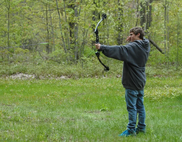 Teenage boy shooting compound bow with arrow in the scene — Stock Photo, Image