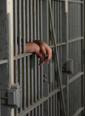 mans hands behind bars in jail or prison