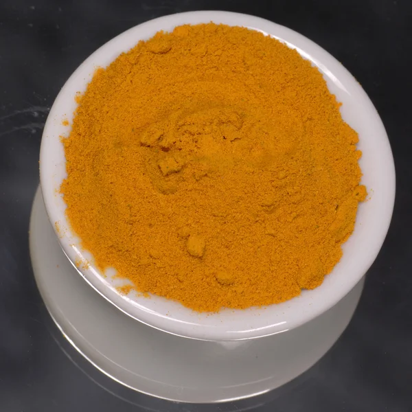 Ground tumeric in white dispenser on black background — Stock Photo, Image