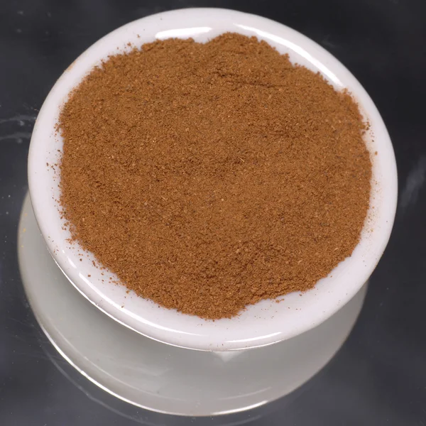 Ground cinnamon in white dispenser on black background — Stock Photo, Image