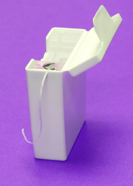 Dental floss in white container on purple background — Stock Photo, Image