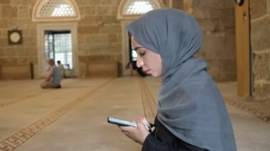 Camide namaz kılan, genç Müslüman bir kadın İslami kutsal telefon okuyor.