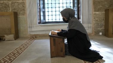 Allah 'a kutsal kitap okuyan, tarihi camide Kur' an okuyan Maskeli Müslüman kadın.