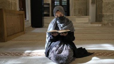 Allah 'a dua eden Maskeli Müslüman kız camide Kuran okuyor.
