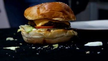 Sırtı bulanık tek hamburger menüsü, ekmek ve köfteli katmanlı hamburger görüntüsü, arka planda lezzetli fast food 'un yavaş çekim görüntüsü