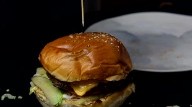 Yumuşak bir hamburgerin içine çubuk sokmanın yavaş çekim görüntüsü, lezzetli bir fast food servisi hazırlamak, hamburger menüsü ekmek ve köfte katmanlarından oluşuyor.