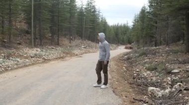 Ormanda asfalt yolda otostop çeken genç adam, ara sıra kapüşonlu adamın el hareketlerini durdur, dağ yolunda aracı durdur.