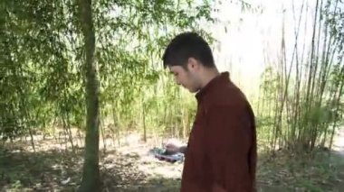 Ormanda gezinirken telefona bakan genç adam, ağaçların arasında cep telefonuyla yolunu bulan kişinin görüntüsü, orman gezisinde telefonu kullanan genç adam.