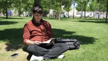 Sırtı ağaca dönük kitap okuyan genç bir adam, çimlerin üzerinde romanını okuyan bir çocuk, güneşli bir tatil gününde parkta vakit geçiren bir adam.