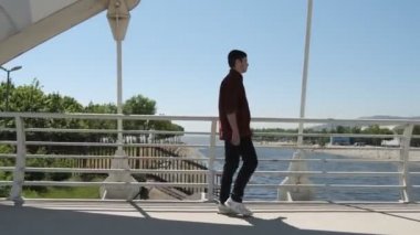Beyaz korkuluk köprüsünde yürüyen yakışıklı bir adam, güneşli bir günde bir öpücükle nehri geçerken, yolcu köprüsünü geçerken.