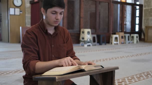 Młody Człowiek Siedzący Kolanach Czytający Koran Drewnianym Uchwycie Wewnątrz Meczetu — Wideo stockowe