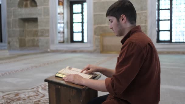 Joven Sentado Rodillas Leyendo Corán Soporte Madera Dentro Mezquita Ángulo — Vídeo de stock