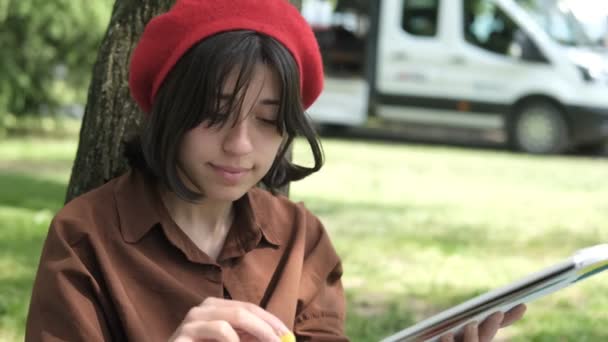 木に背を向けて美しい女性の絵のイメージ 緑の公園の赤い帽子の女性のイメージ 白いキャンバスの油彩画 — ストック動画