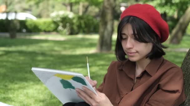 美丽的女人背对着树画画 绿色公园戴着红帽子的女人画像 白色帆布上的油画 — 图库视频影像