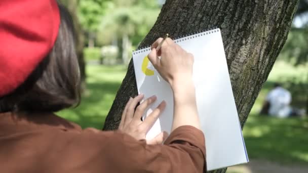 女性は木にキャンバスをもたせて絵を描き アーティストは自然を描き 外側の平均にブラシで描いています — ストック動画