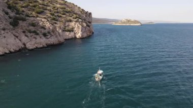 Koyda yüzen balıkçı teknesinin drone görüntüsü, mavi denizde gündüz beyaz tekne, yaz günü tekne yolculuğu, kıyıya yakın hareket eden tekne.