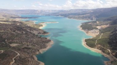 The view of the dam in the mountains taken with a drone, the aerial picture of the large water lake, dam in the middle of green fields
