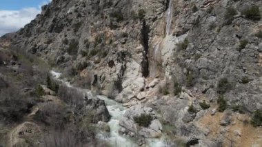 Kahverengi kayalar arasında akan suyun görüntüsü, vadideki dereye dökülen şelalenin görüntüsü, eğimli karalar arasında akan şelale akıntısının görüntüsü.