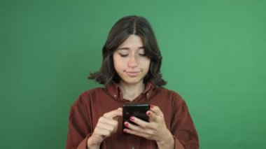 Image of young girl looking at phone in hand, girl smiling at things shes looking at, facial expression of young woman in front of green curtain