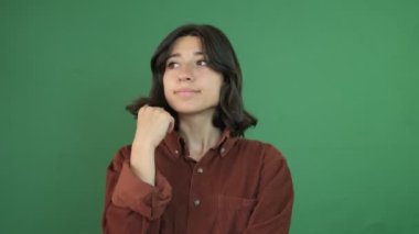 Beklerken genç bir kadının yüz ifadesi, saçlarıyla oynayan ve etrafına bakınan bir kızın görüntüsü, yeşil perdenin önündeki genç kadının yüz ifadesi.