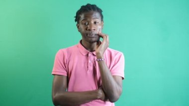 Image of black male thoughtfully putting his hand to his head, models solitary thinking gestures, image of emotions and facial expressions taken in front of the green curtain