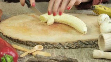 Tahta kesme tahtasında sarı muzu dilimleyen bir kadın resmi, tematik doğal ürünler masasında meyve hazırlama, ahşap sunum tabağında dilimleme işlemi