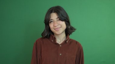 Bir gözünü kırpan güzel bir kız, yeşil ekranın önünde yüzünü anlamlı mesajlarla kullanıyor, yeşil perdenin önünde genç bir kadının yüz ifadesi.