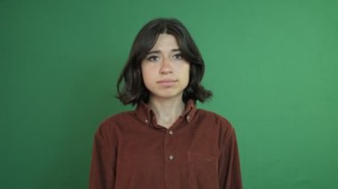 Kızgın yüz ifadesi olan bir kadın, yüzü asık güzel bir kız imajı, yeşil perdenin önündeki genç bir kadının yüz ifadesi.