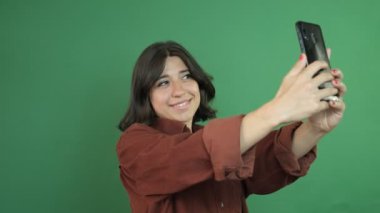 Image of girl taking selfie with phone, cheerful girl taking photo with phone, facial expression of young woman in front of green curtain