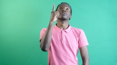 Pointing with finger up, black teenager pointing to the top of the screen with his left hand, show body language and facial expressions in front of a green screen