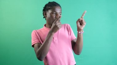 Pointing to left corner, black teenager pointing to the left of the screen with both hands, show body language and facial expressions in front of a green screen