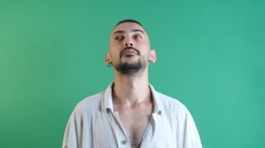 Young mans huffing and puffing facial expression, models solitary thinking gestures, image of emotions and facial expressions taken in front of the green curtain
