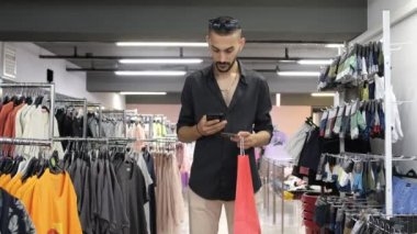 Show your phonescreen in centre, young man show green screen in shopping store, image of shopping from the phone in the clothing aisle