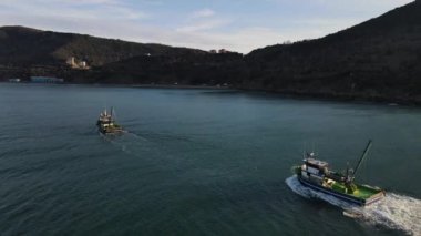 Drone view of small ship foaming in the sea, fishing boat fishing from the sea with nets, colorful boats on turquoise water