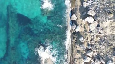 Drone view of the crystal clear sea waters of Kyrenia, turquoise color of the open sea, rocks and the natural beauty of cyprus with waves crashing on the beach