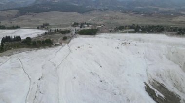 Drone view of Pamukkale travertines, natural beauty consisting of waterfalls and swimming pool with white minerals in Turkey, white travertines on one side of the mountain