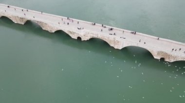 The drone images of vehicle traffic passing over the bridge over the river, road crossing over water, movements of vehicles in traffic