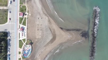Drone view of the beach by the sea, waves hitting the beach, coastal driveway passing through the coastline