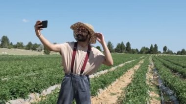 Man taking selfie in garden, young farmer in hat taking photo in green garden, taking a selfie in a row of tomatoes