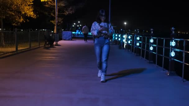 女性の夜のウォーキング 仕事のリラクゼーション活動の後のカラフルな光の下で夜散歩 — ストック動画