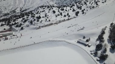 Kayak alanında kayak yapan insanların insansız hava aracı görüntüsü, dağ yamacına kurulmuş kayak merkezinden kayak yapan tatilcilerin insansız hava aracı görüntüsü.