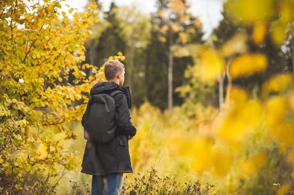 Egy tinédzser fiú sötét kabátban és hátizsákkal áll az őszi parkban háttal a kamerának. Fogalom digitális méregtelenítés. Őszi séták. — Stock Fotó