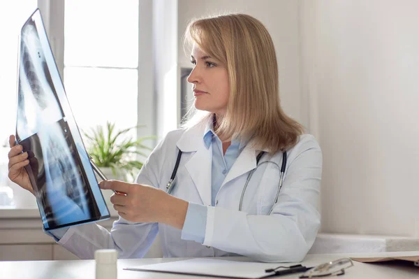 Una doctora seria y reflexiva examina una radiografía de los pulmones y explica el diagnóstico. Concepto de telemedicina, consultas remotas en línea y visita virtual al hospital — Foto de Stock