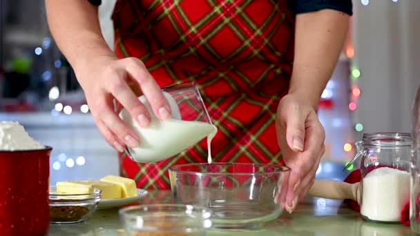 A nők kezek öntsük a tejterméket az üvegből egy tálba, hogy előkészítse a tésztát a otthonos konyha díszített karácsonyra. Konyha díszített karácsonyi fények — Stock videók