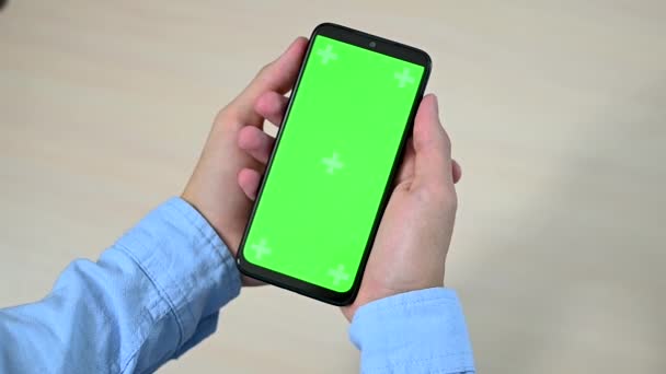 Close-up van een jonge man of tieners hand met een mobiele telefoon met een verticaal groen scherm over een tafel Focus op het scherm chroma toets, — Stockvideo