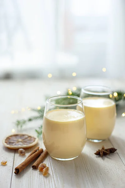 Dwie szklanki ajerkoniaku na białym drewnianym stole przy oknie. Świąteczny deser. Słodki zimowy koktajl. Zdjęcie pionowe Selektywne ustawianie ostrości Obrazy Stockowe bez tantiem