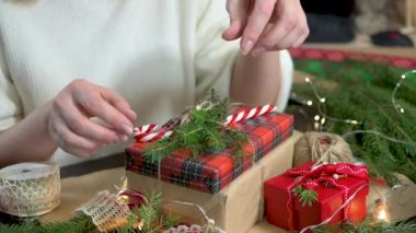 Kadınların elleri Noel hediyesiyle kutuyu süslüyor. Dekorlu masa ve dekorasyon malzemeleri. İşlem dikiş işidir. Seçici odak