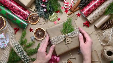 Kadınların elleri Noel hediyesiyle kutuyu süslüyor. Dekorlu masa ve dekorasyon malzemeleri. İşlem dikiş işidir. Seçici odak