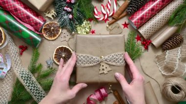 Kadınların elleri Noel hediyesiyle kutuyu süslüyor. Dekorlu masa ve dekorasyon malzemeleri. İşlem dikiş işidir. Seçici odak