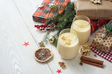 Noel hediyelerinin yanındaki beyaz tahta masada iki bardak eggnog. Tatlı yumurta tatlısı. Noel kahvaltısı.